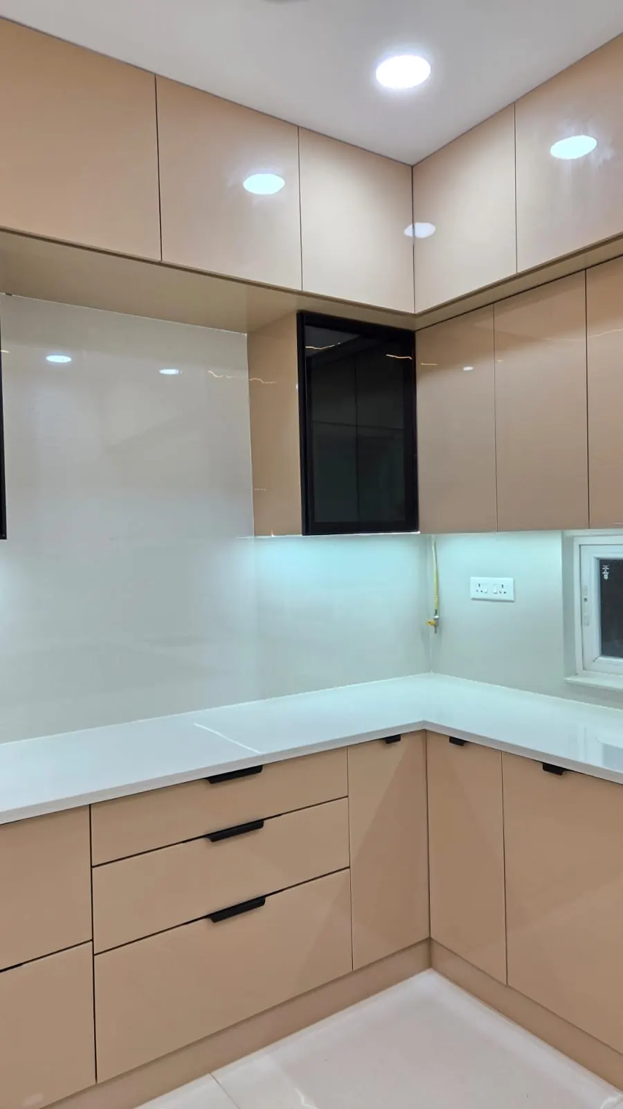 L-shaped modular kitchen with beige gloss shutters, tall wall cabinets and under-cabinet lights