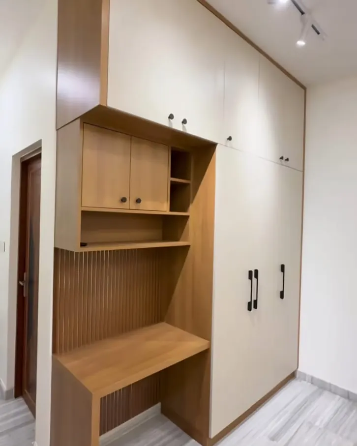 Floor-to-ceiling white wardrobe beside a wood-finish study desk with open shelves